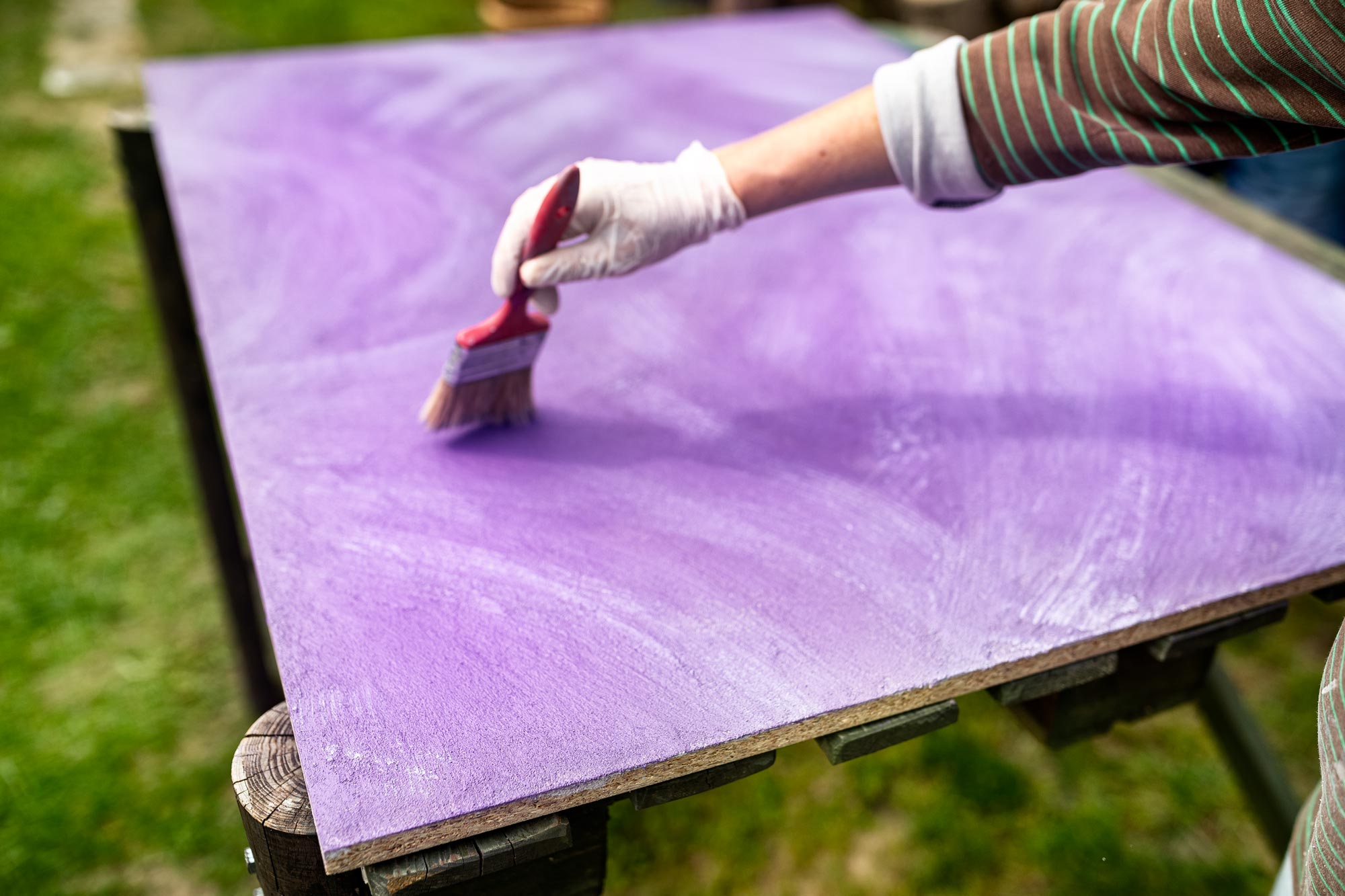 Building photographic backgrounds. A hand with a painting brush is shown, blurred in the background a half painted piece of wood.