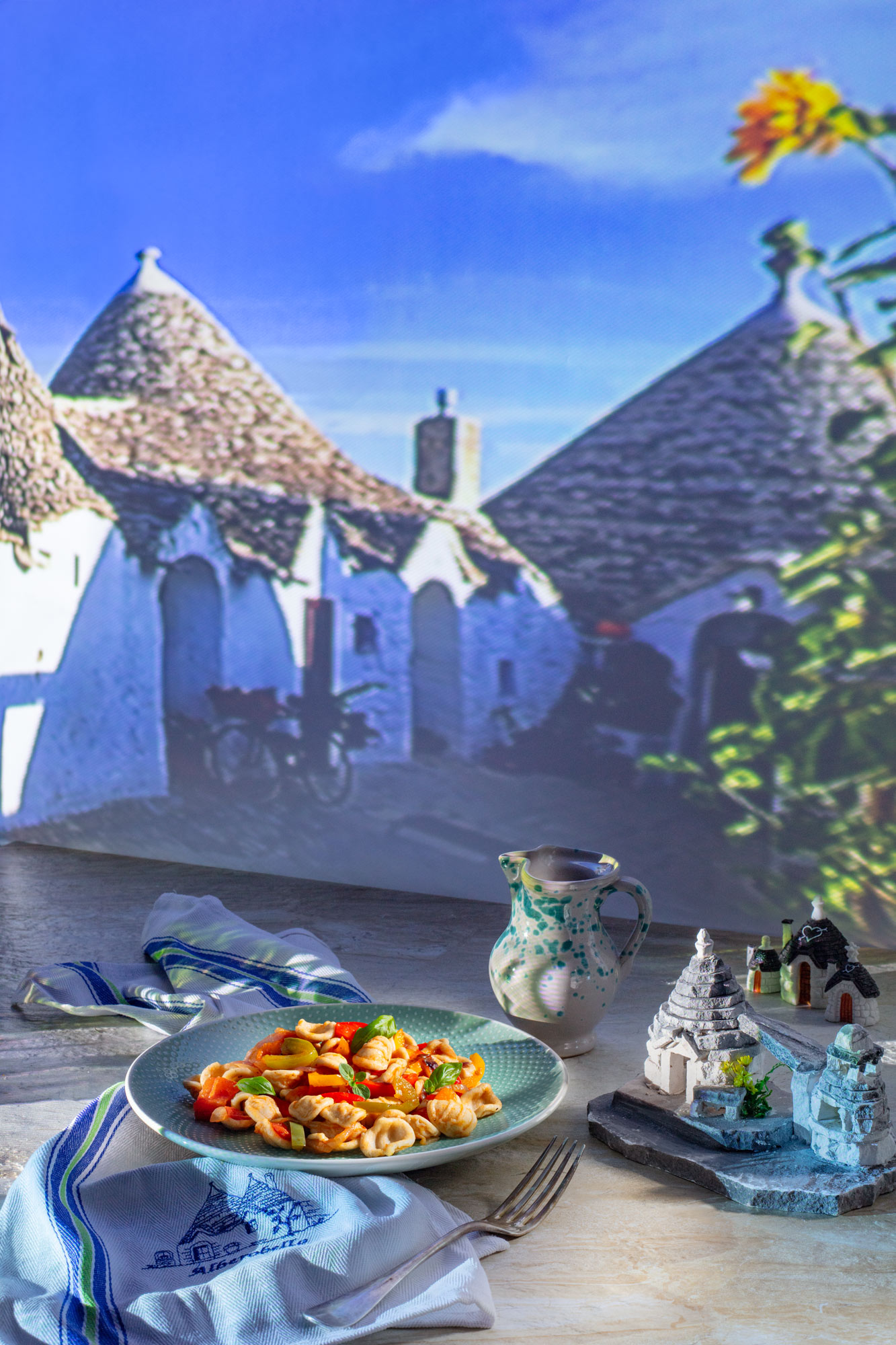 A dish of Orecchiette pasta with peperonata sauce. In the backgroun a view of traditional Trullis, houses popular in the Apulia region of Italy. Small models of Trullis surrounding the dish. 